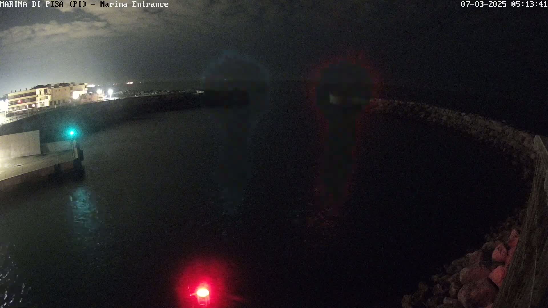 A nighttime view of a dark harbor with faint lights reflecting on the water,  illuminated by a green and red navigational light.