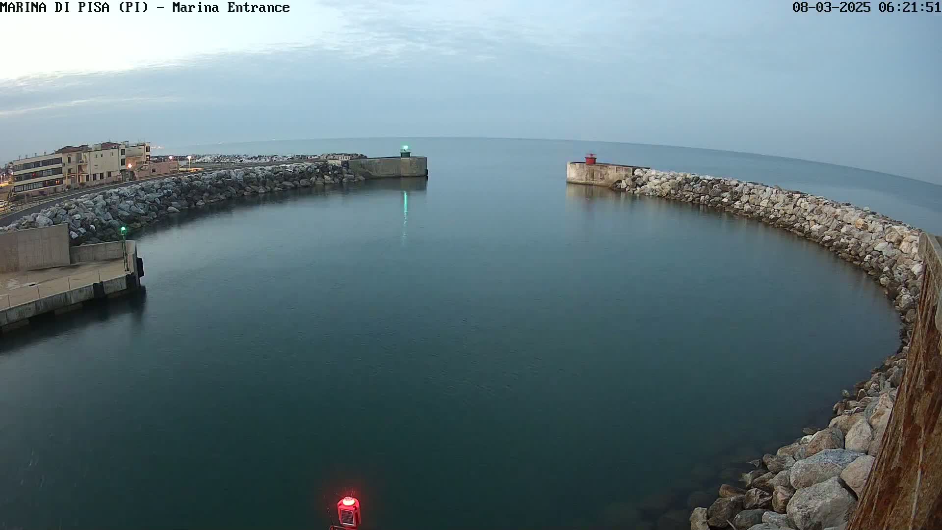 A calm, overcast day reveals a harbor entrance defined by rock walls, with a building visible in the distance.