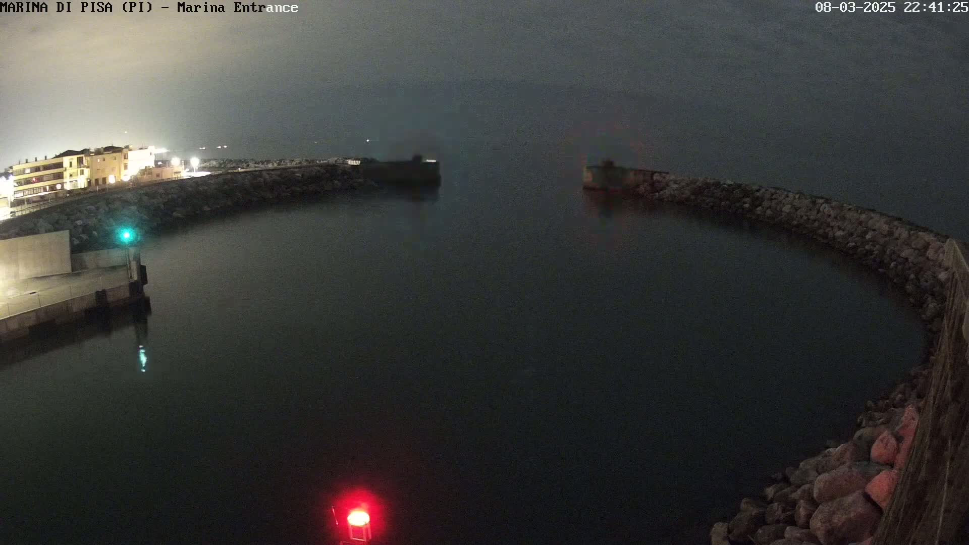 A nighttime, overcast view of a calm harbor entrance with a building visible in the background.