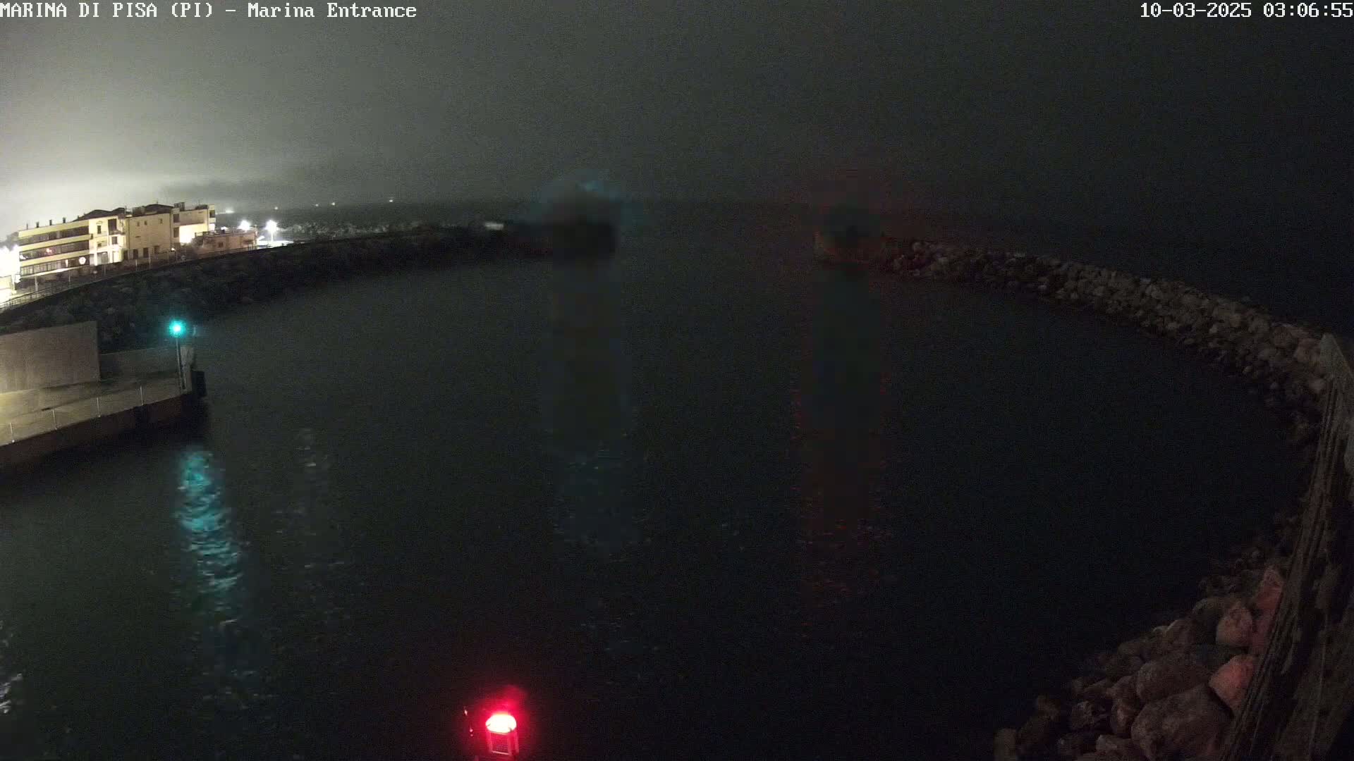 A dark, nighttime view of a harbor entrance with calm water, under foggy or overcast conditions.