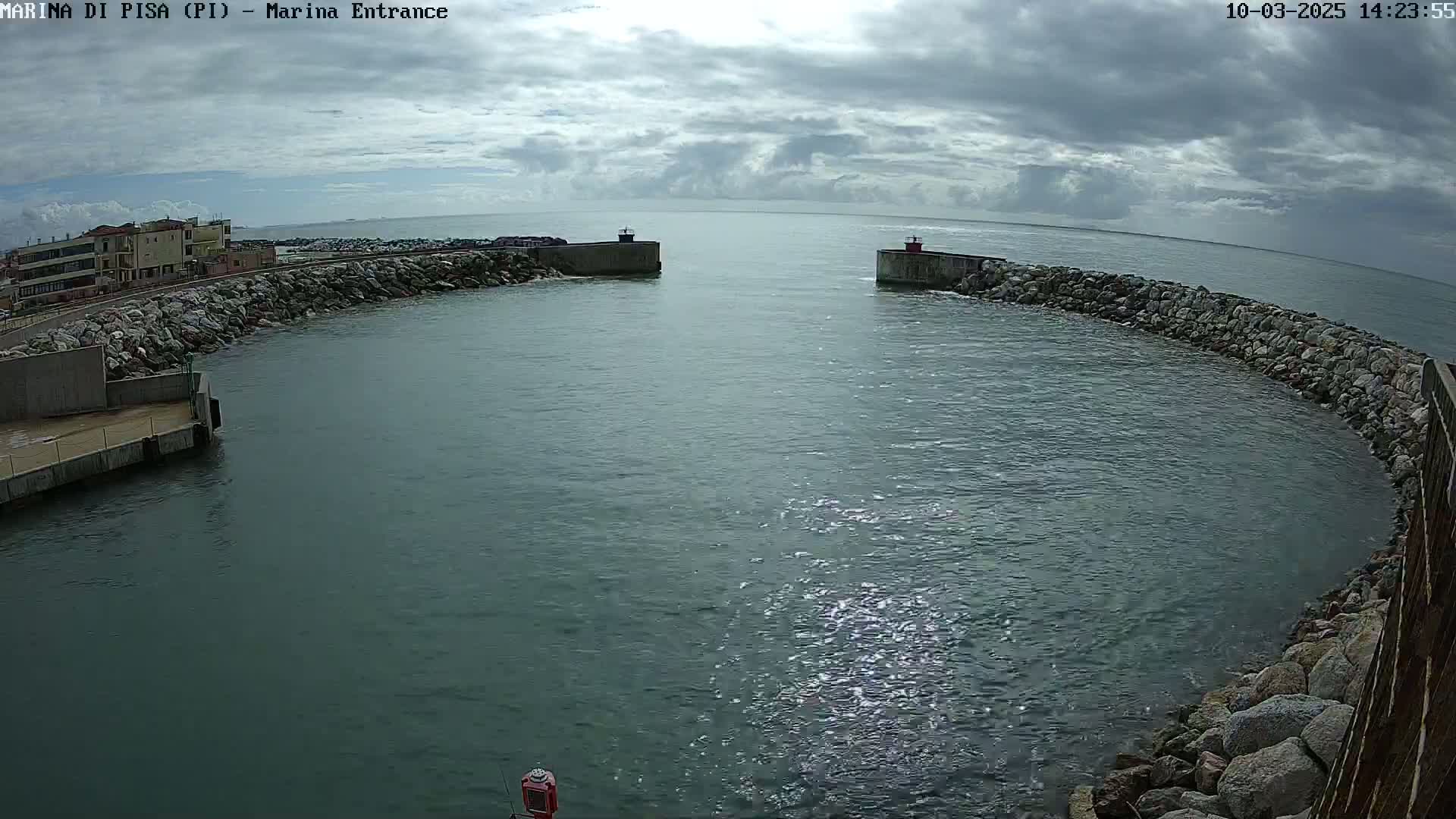 A harbor entrance with calm, dark-green water under a mostly cloudy sky is seen from a high vantage point.
