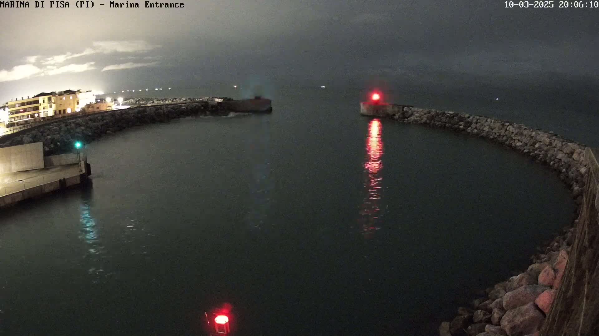 A nighttime view of a harbor entrance with calm water, illuminated by harbor lights under a dark, cloudy sky.