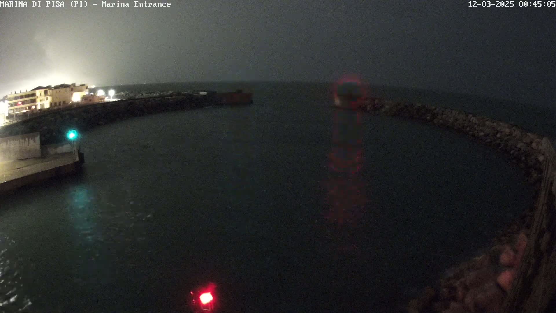 A nighttime view of a harbor entrance with choppy water under an overcast sky.