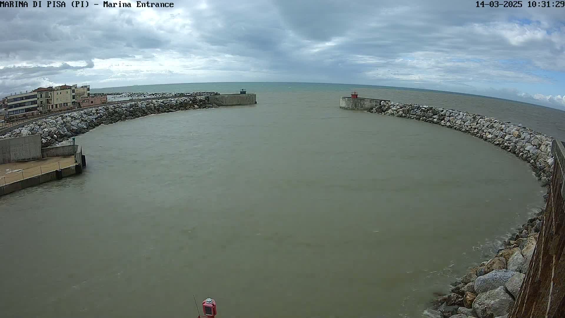 A harbor entrance with calm, murky water is partially enclosed by rock walls under an overcast sky.