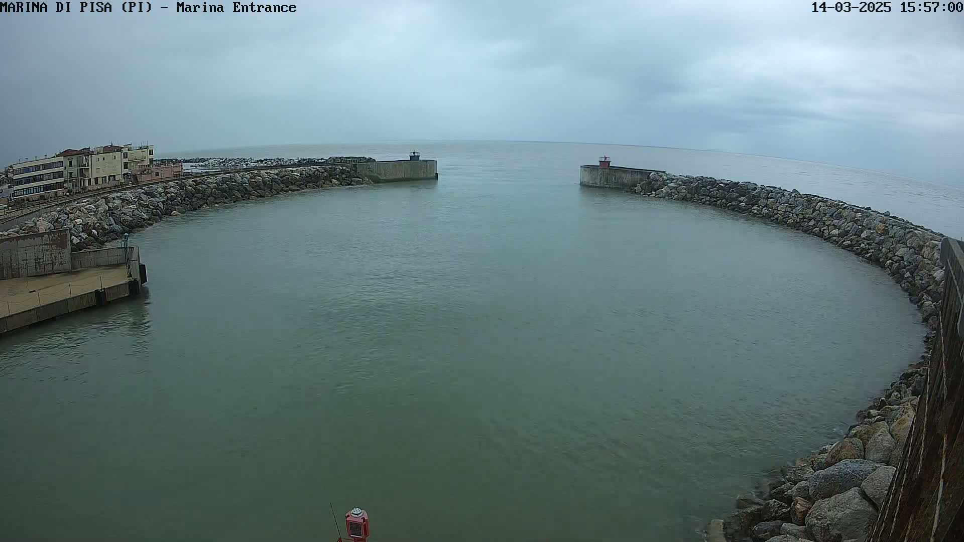 A harbor entrance with calm, greenish-gray water is enclosed by rock walls, under an overcast sky.