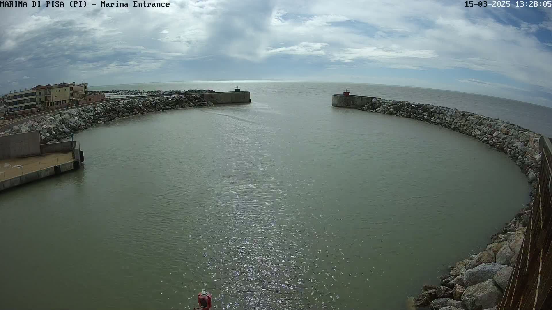 A calm harbor entrance with cloudy skies is seen from an elevated vantage point, showing rock walls and buildings in the distance.