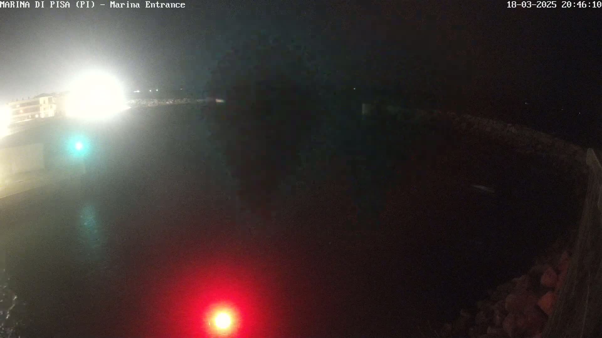 A nighttime view of a dark body of water, illuminated by a bright light source in the distance and a red light closer to the camera.