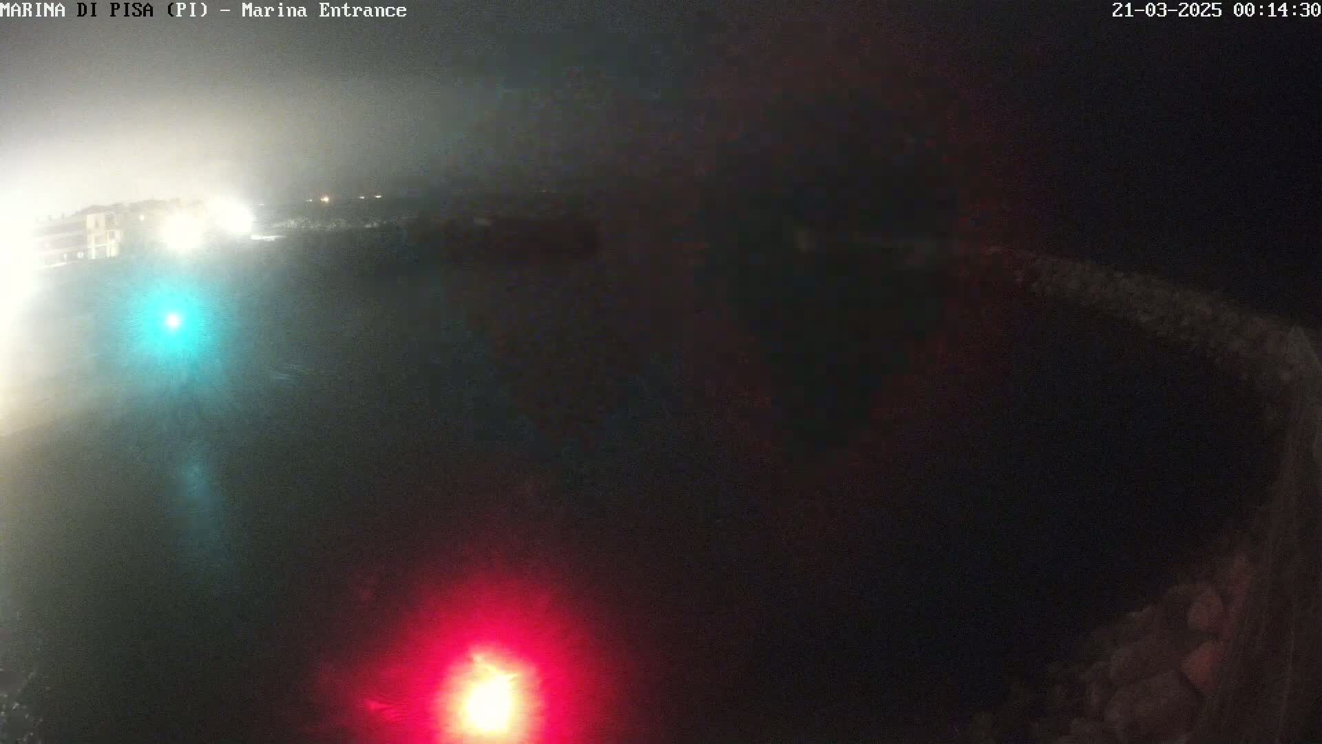 A dark, nighttime scene shows a hazy, possibly foggy or misty, area with faint lights in the distance and a red light at the bottom.