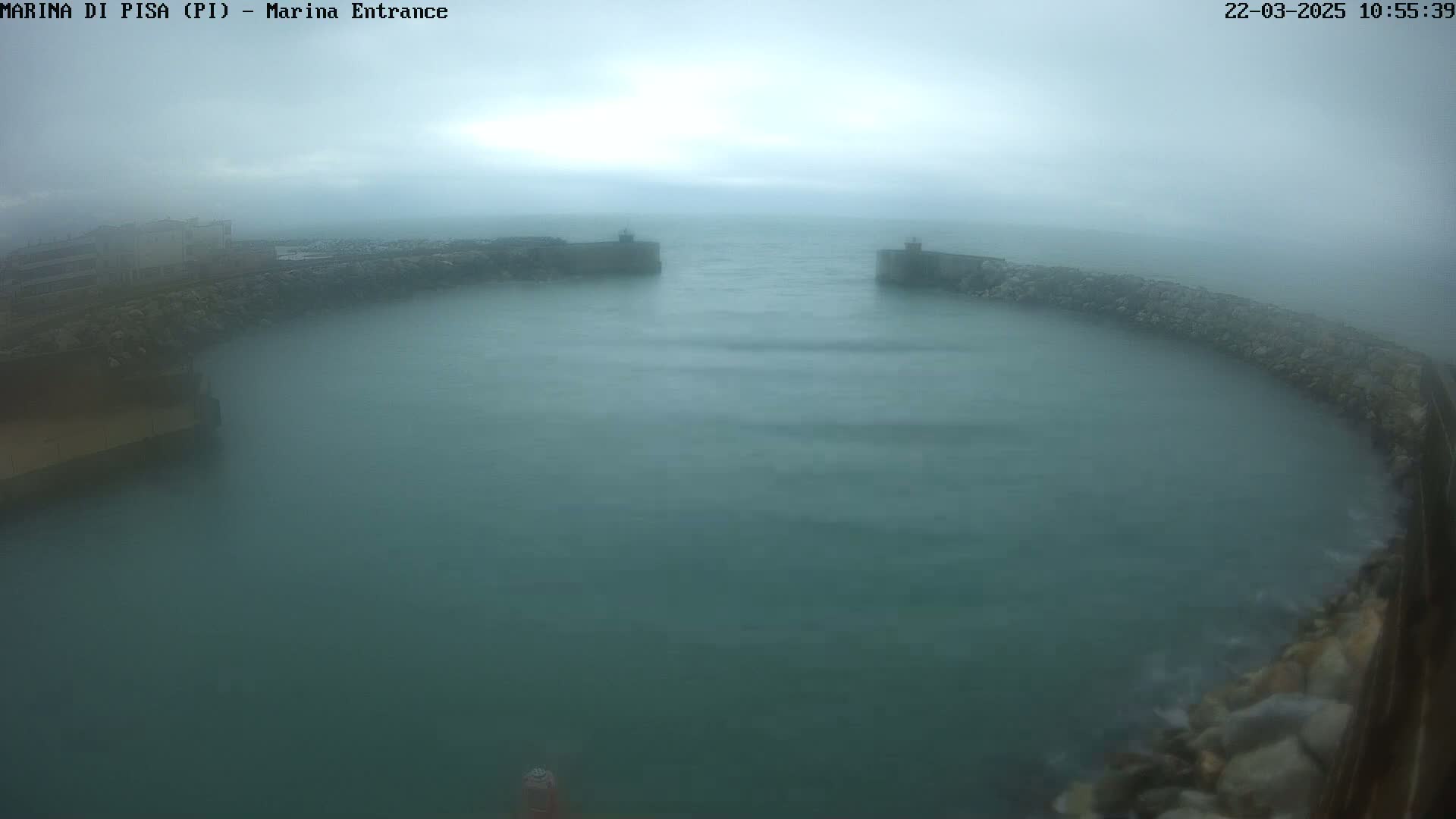A foggy harbor entrance with choppy water is seen from an elevated position.