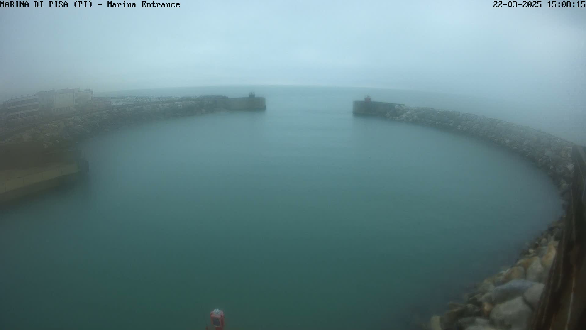 A foggy view of a harbor entrance with calm, greenish water enclosed by stone walls.