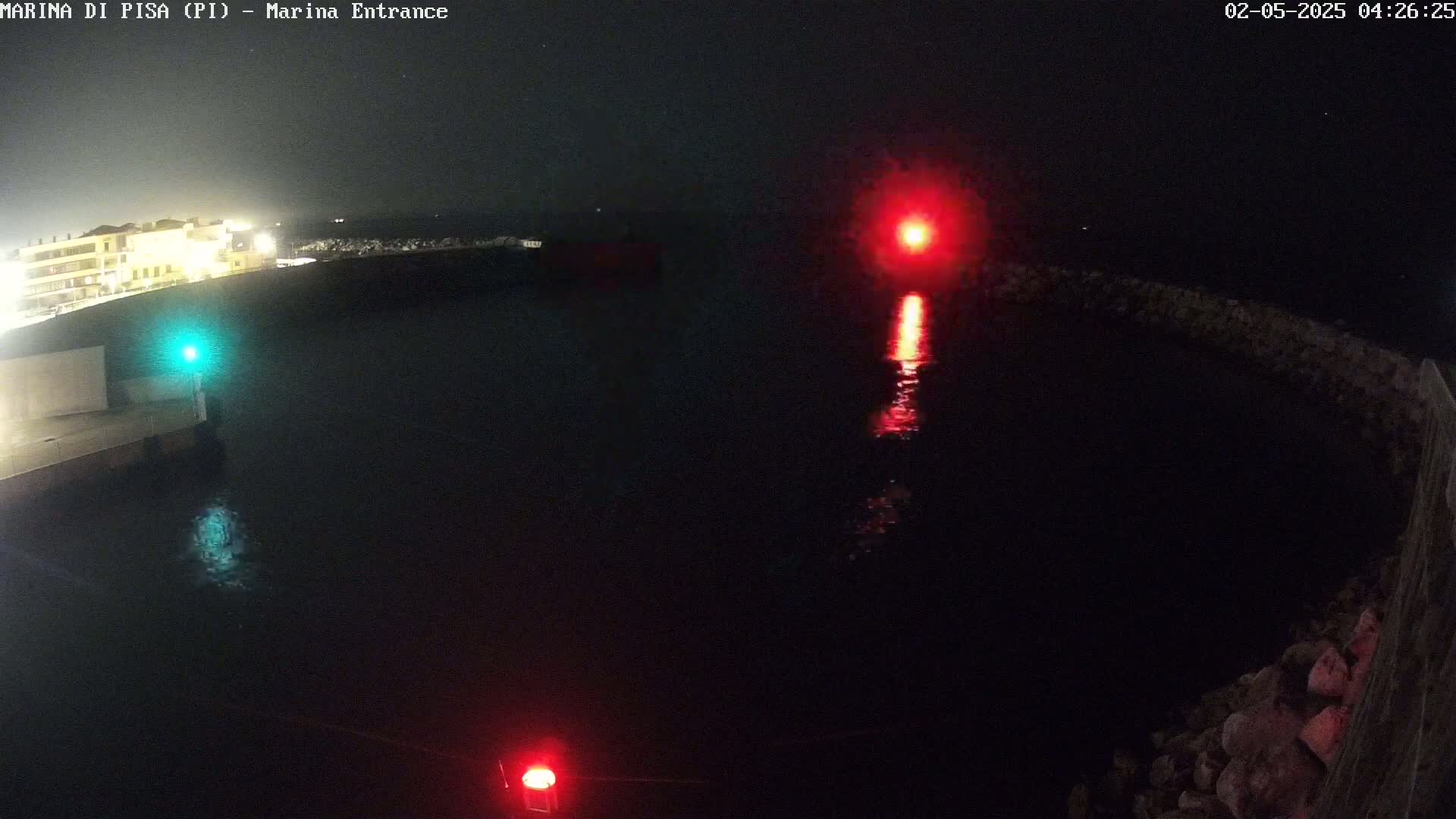 A nighttime view of a harbor entrance with a red and a green light illuminating dark water.