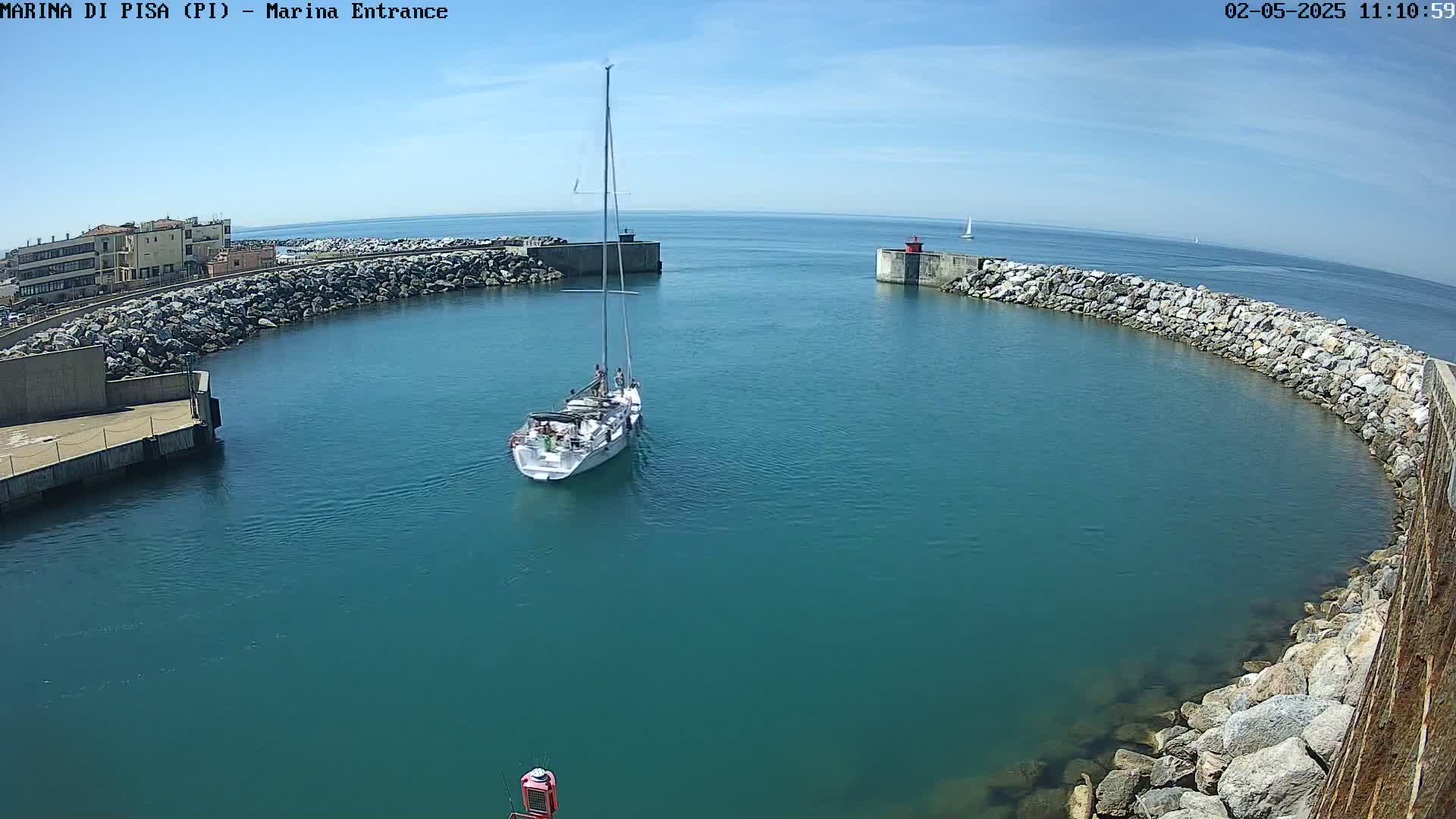 A sailboat enters a harbor on a sunny day, passing between two rock walls.