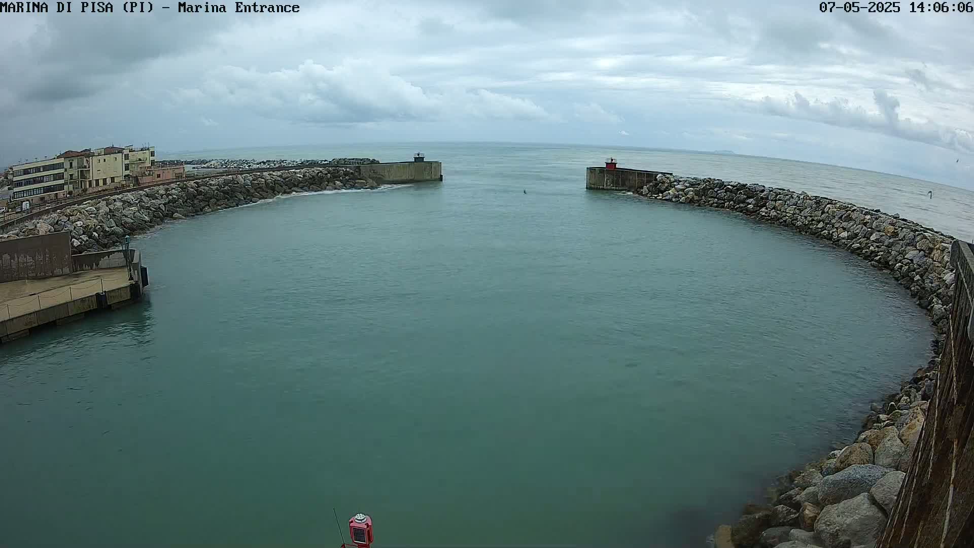 A calm, green body of water is enclosed by stone walls and buildings under a cloudy sky.