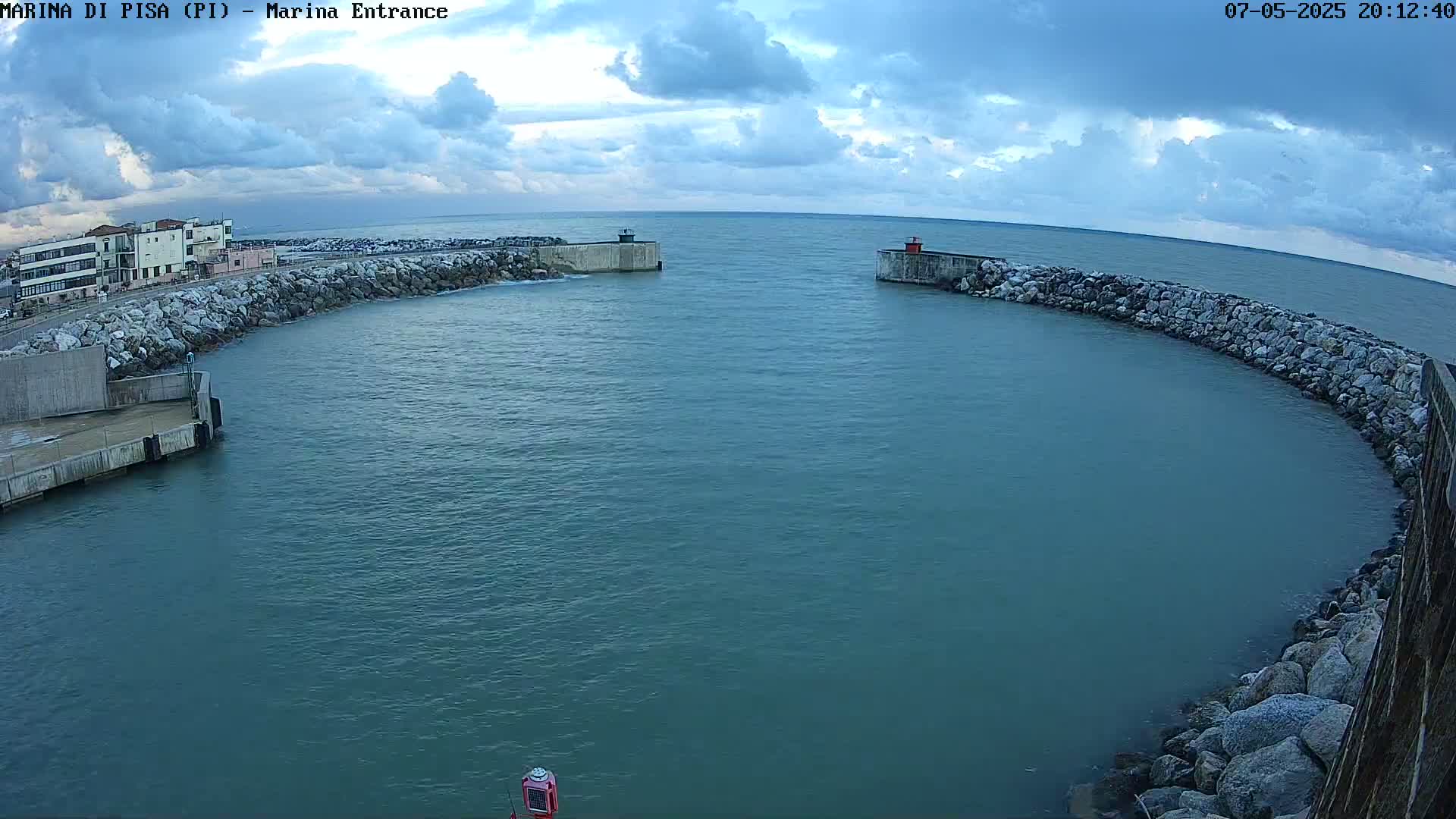 A harbor entrance with calm, dark-blue water under a partly cloudy sky.