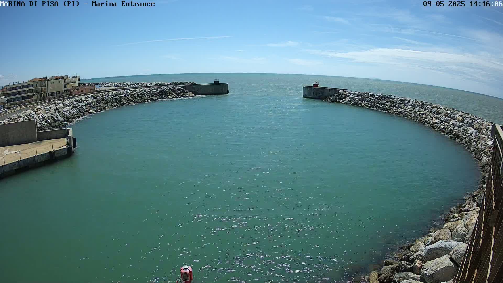A calm, teal-colored body of water is seen nestled between two rocky breakwaters on a sunny day.