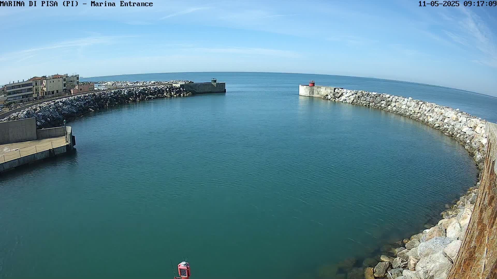 A calm, teal-colored harbor is partially enclosed by rocky walls under a clear blue sky.