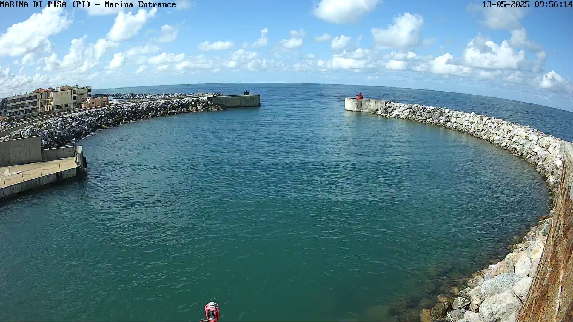 A harbor entrance with calm, teal water is partially enclosed by stone walls under a partly cloudy sky.