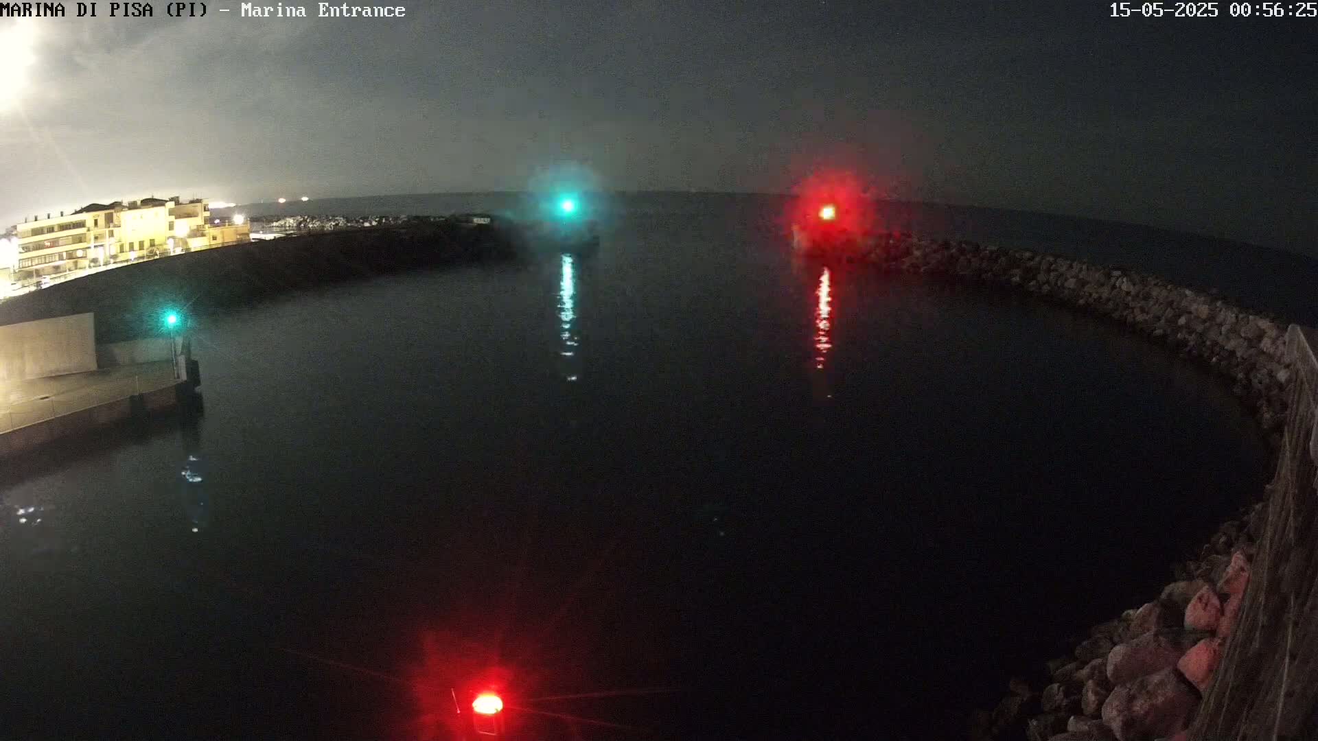 At night, a dark body of water is enclosed by a low stone wall, with a green and red light visible on either side of the entrance.