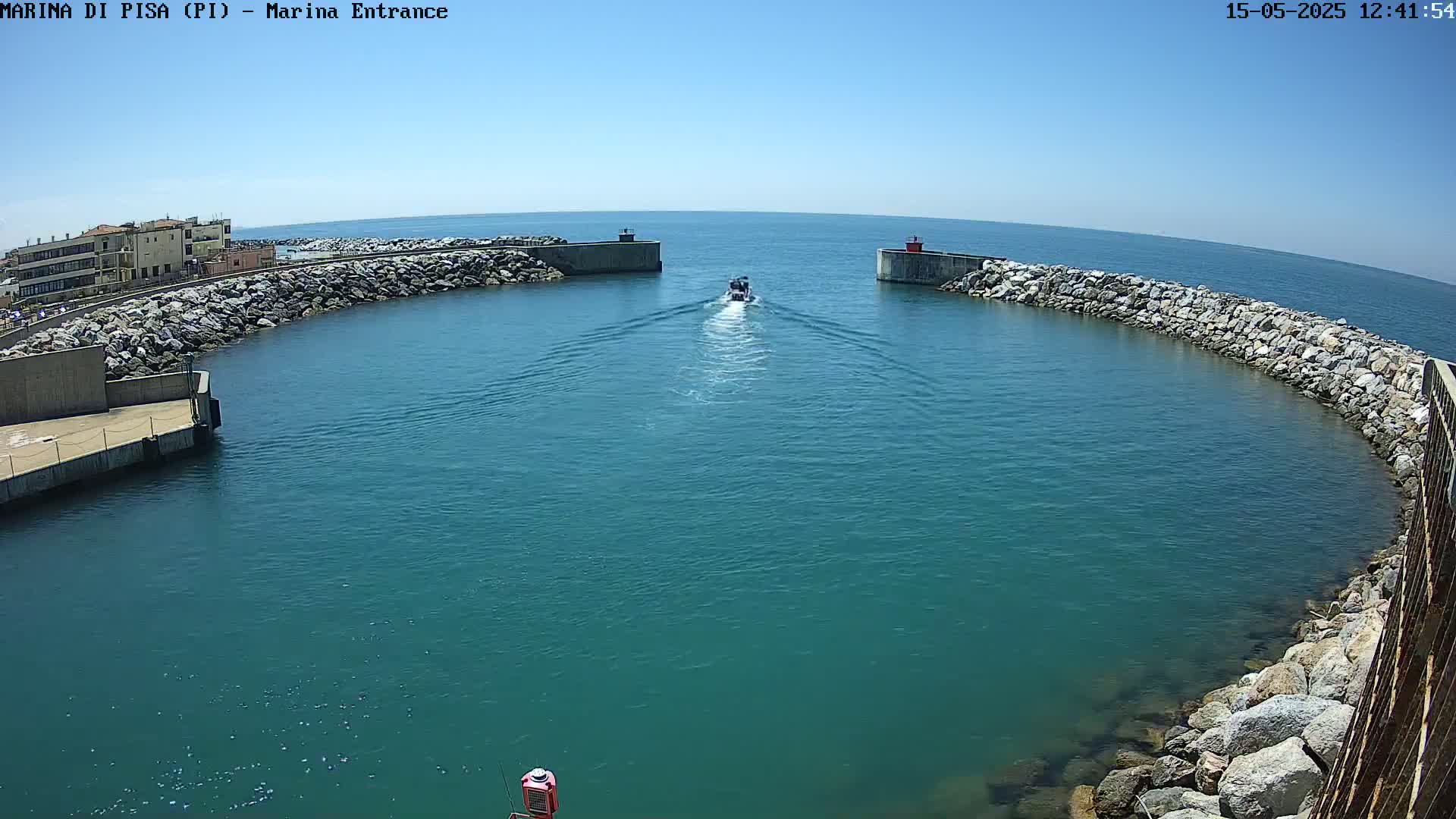 A small boat travels through a harbor entrance on a sunny day, passing between two rock-lined walls.