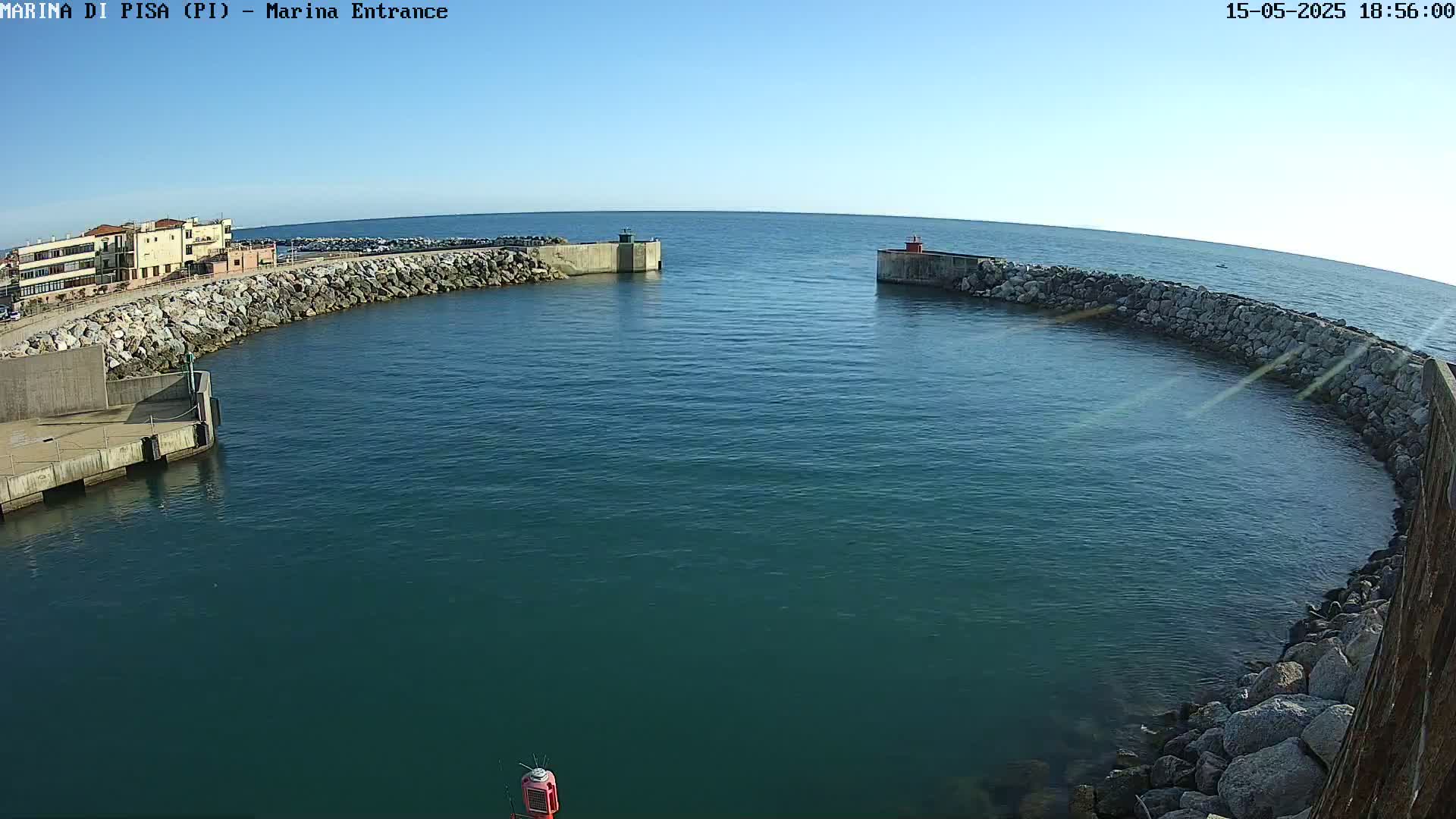 A calm, clear day reveals a marina entrance with a curved stone wall enclosing a tranquil body of dark-blue water.