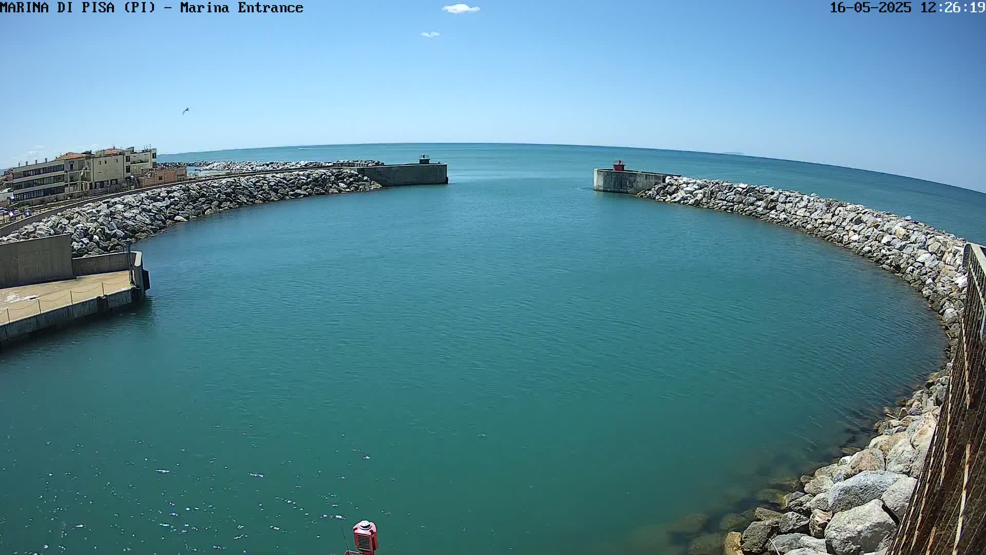 A harbor entrance with calm, teal water is bordered by rock walls under a clear, sunny sky.