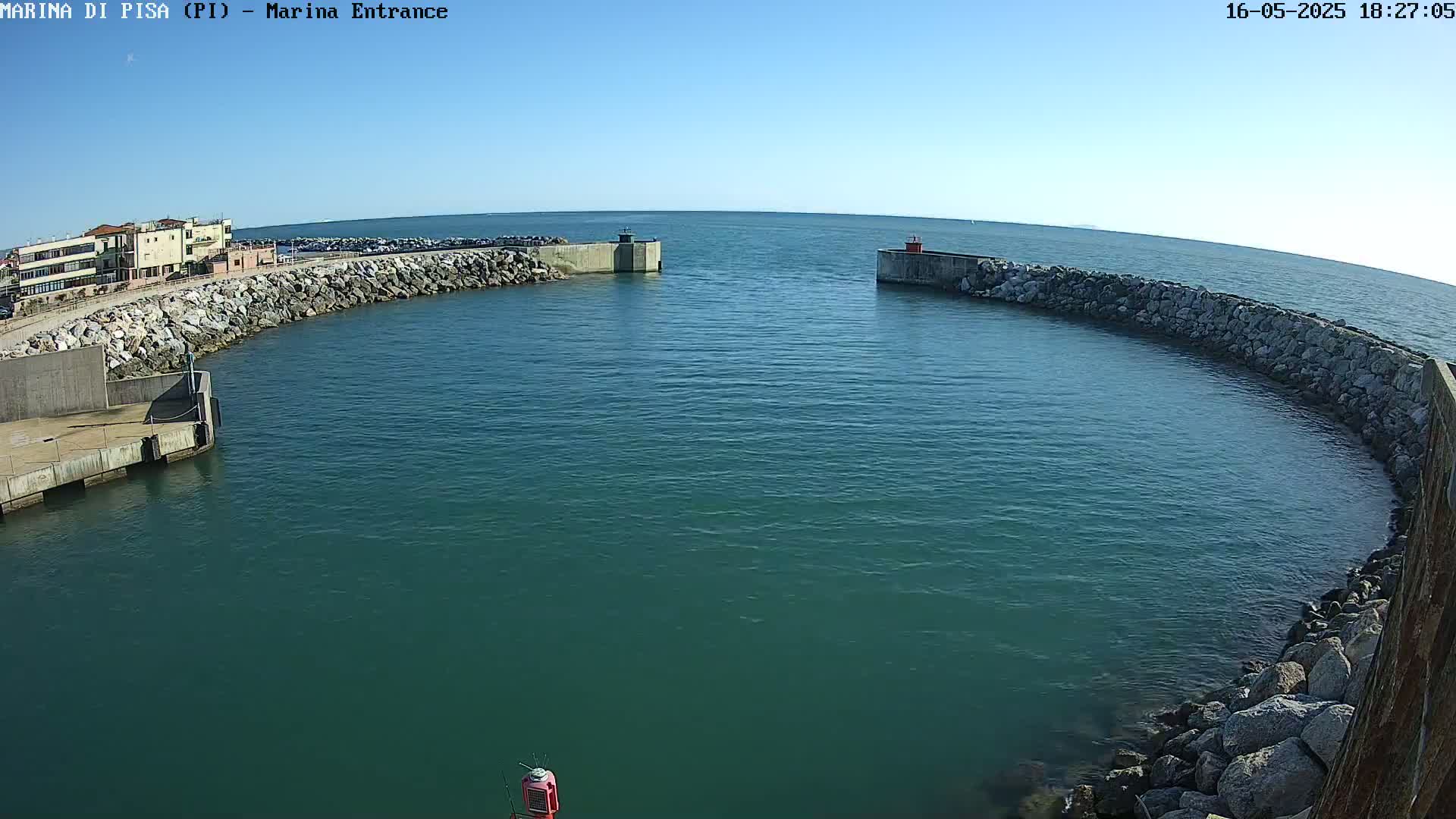 A harbor entrance with calm, teal water is enclosed by rock walls under a clear blue sky.
