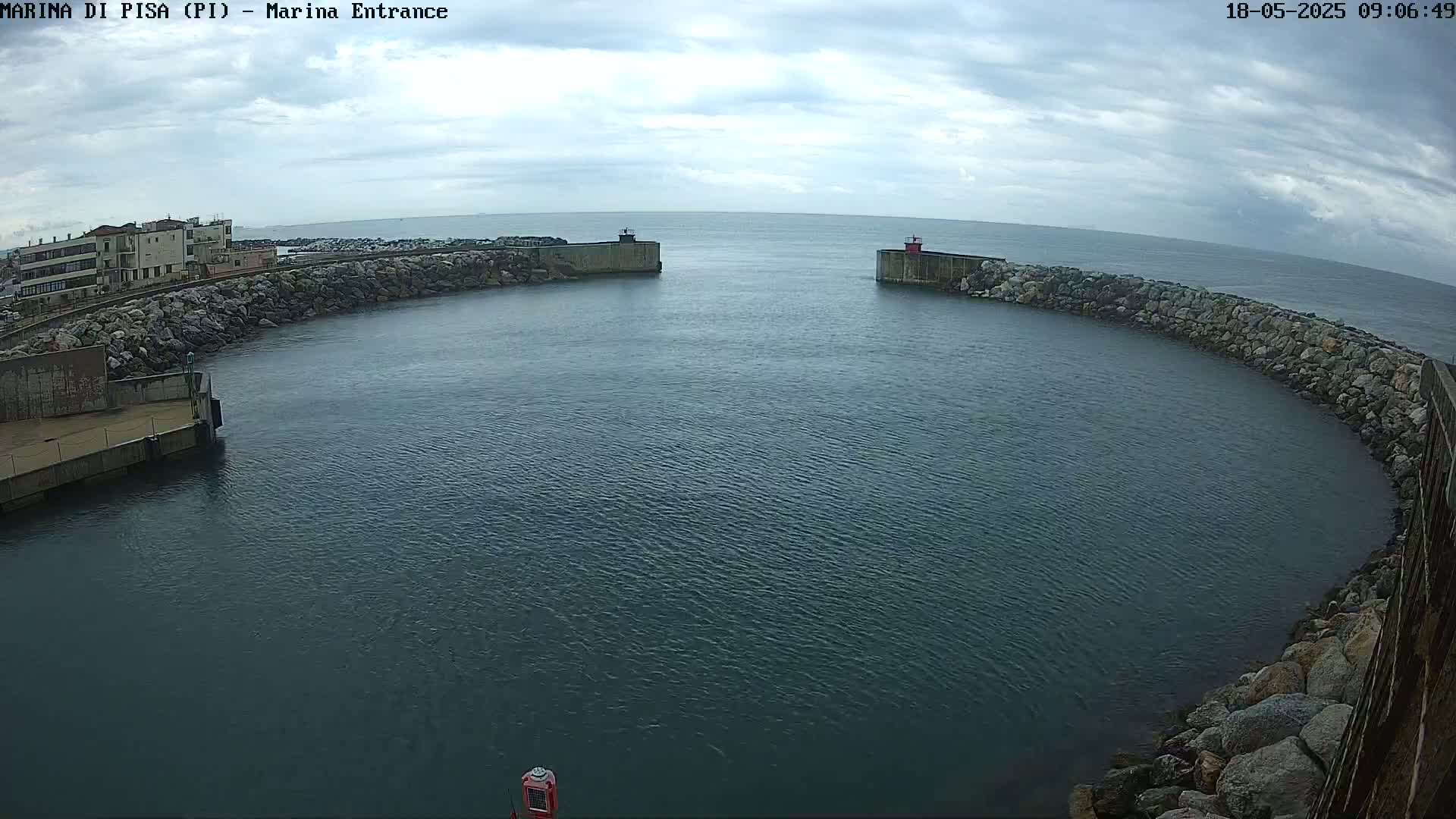 A harbor entrance with calm water under a partly cloudy sky is seen from an elevated vantage point.