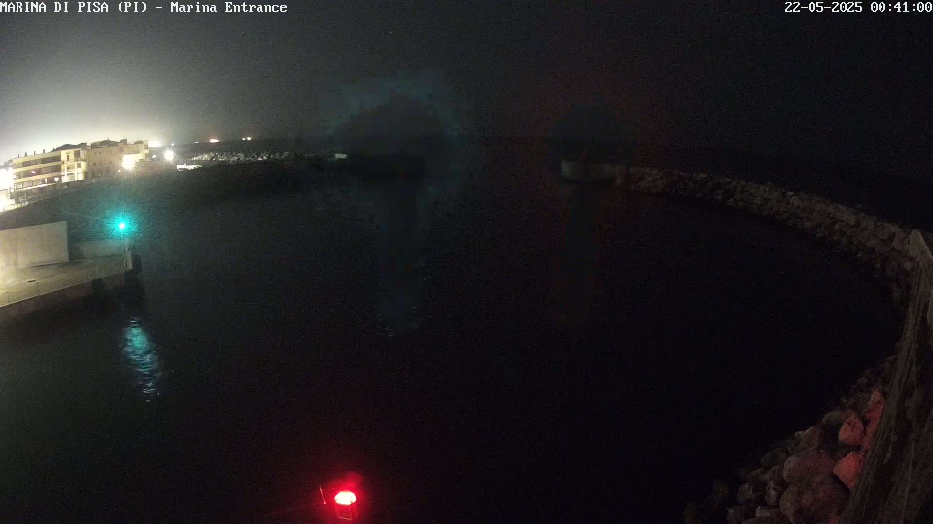 A nighttime view of a dark harbor with a building faintly visible in the distance under a hazy sky.