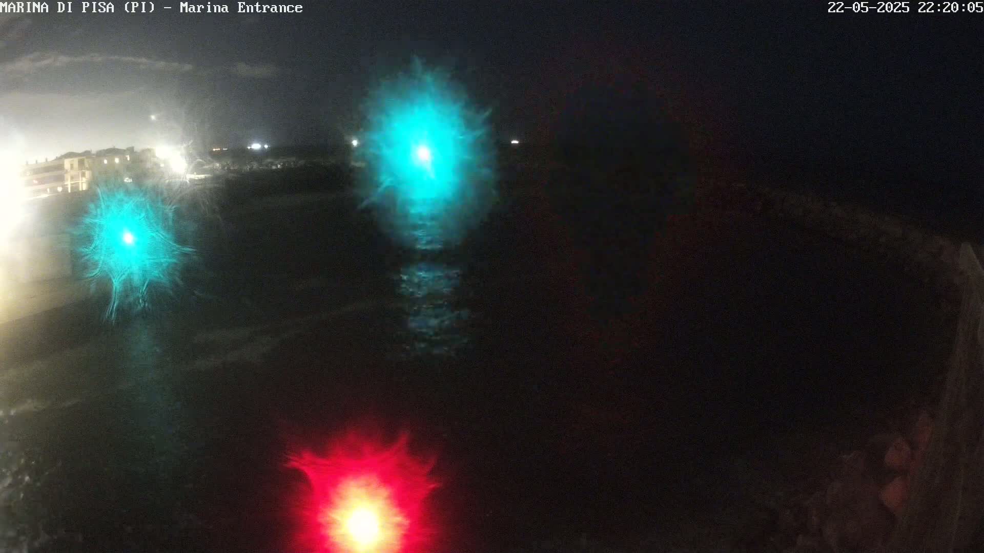 A nighttime, dark view of water with two teal and one red lights reflecting on the surface.