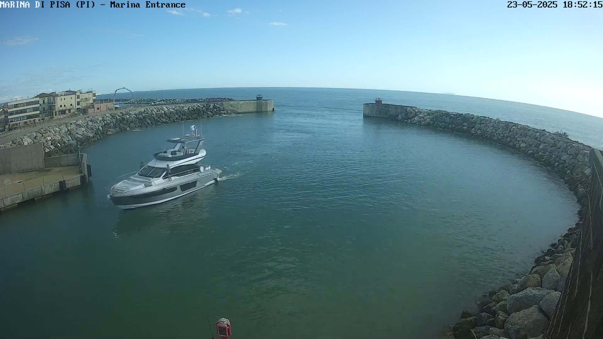 A motor yacht enters a harbor on a calm, sunny day.