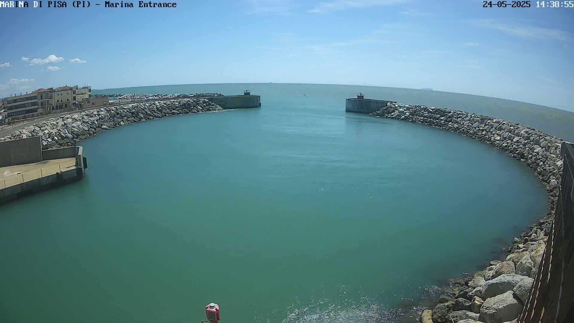 A harbor entrance with calm, teal water is enclosed by stone walls under a sunny sky.
