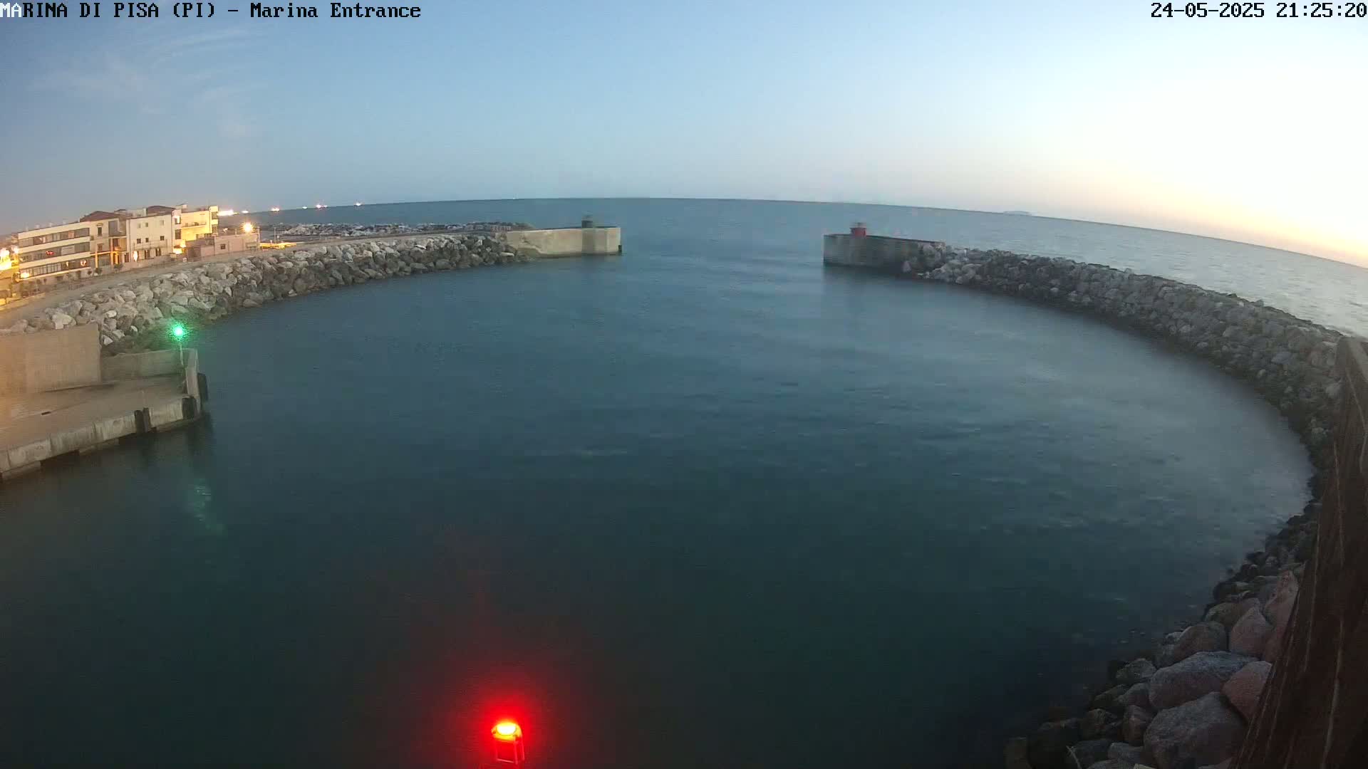 A calm, dark-blue body of water is enclosed by a curved stone wall at dusk, with a building and lights visible in the distance.