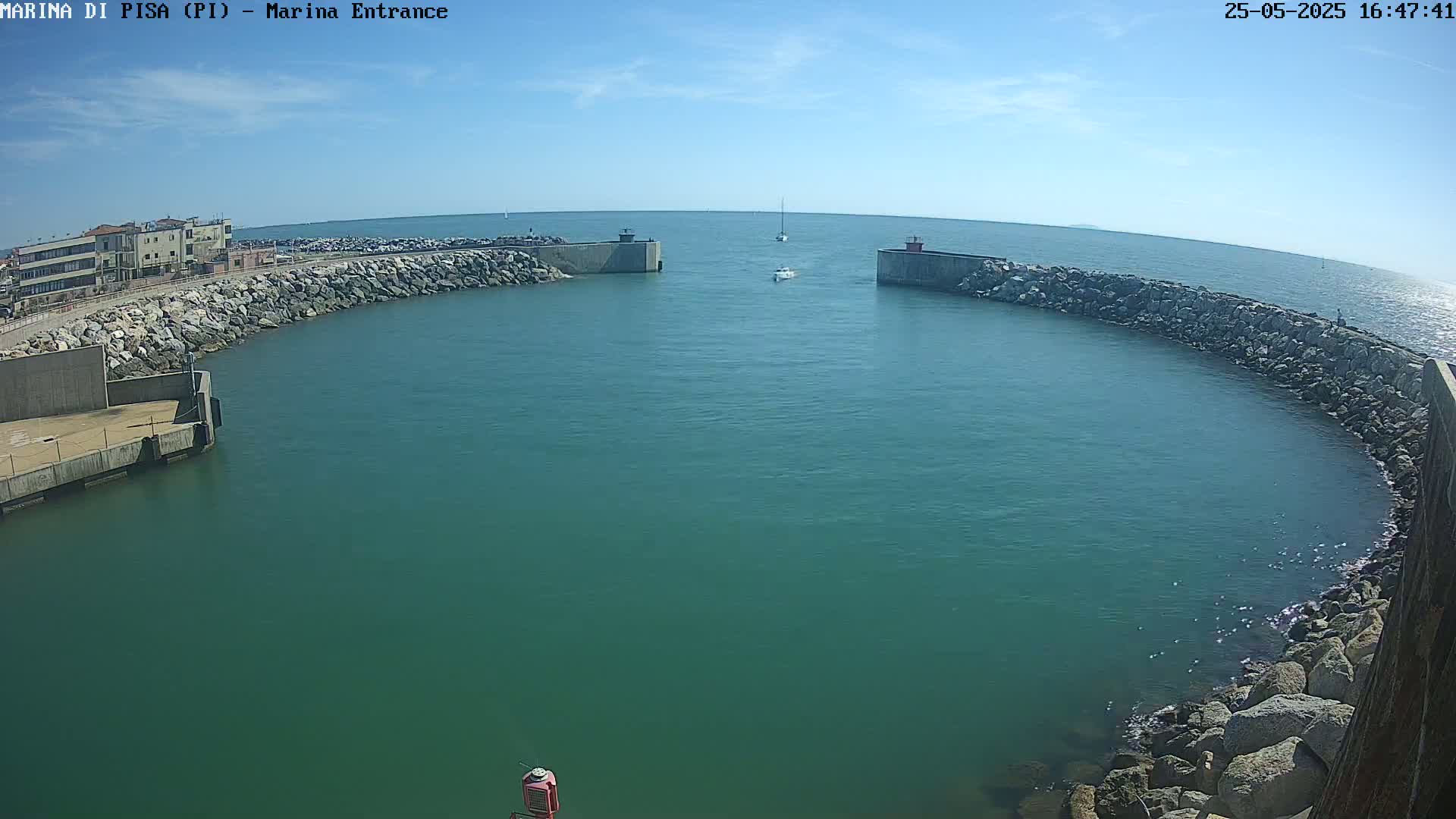 A marina entrance with calm, teal water is partially enclosed by rock walls under a mostly sunny sky.