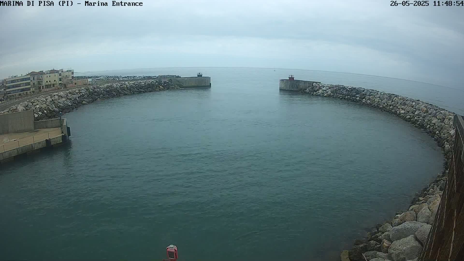 A harbor entrance with calm, dark-green water is enclosed by rock walls under an overcast sky.