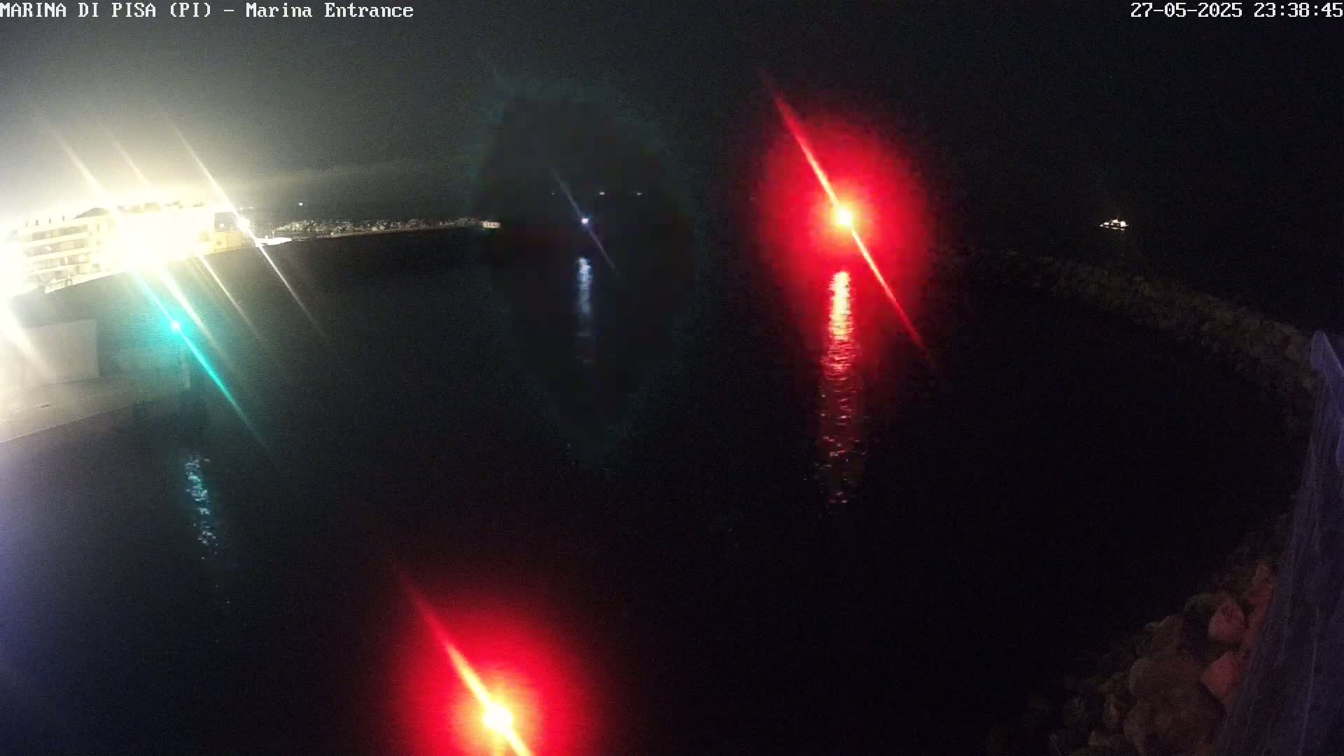 A nighttime view of a marina entrance with red and green navigation lights reflecting on dark water.
