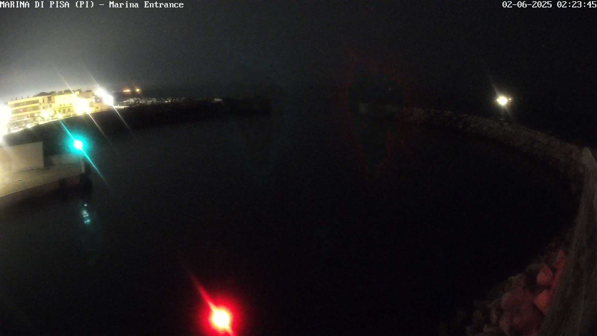 A nighttime, dark view of a harbor entrance with a building lit up in the background and navigational lights visible on the water.