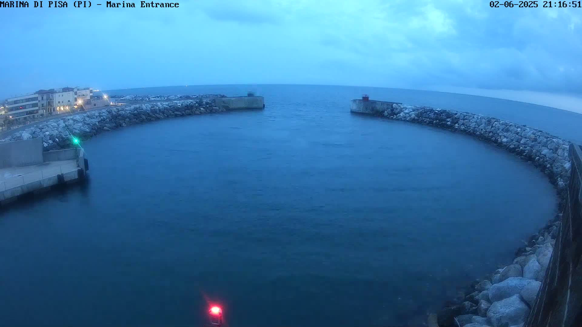 A calm, dark-blue body of water is enclosed by a curved rock wall at dusk, with a small town visible in the background.