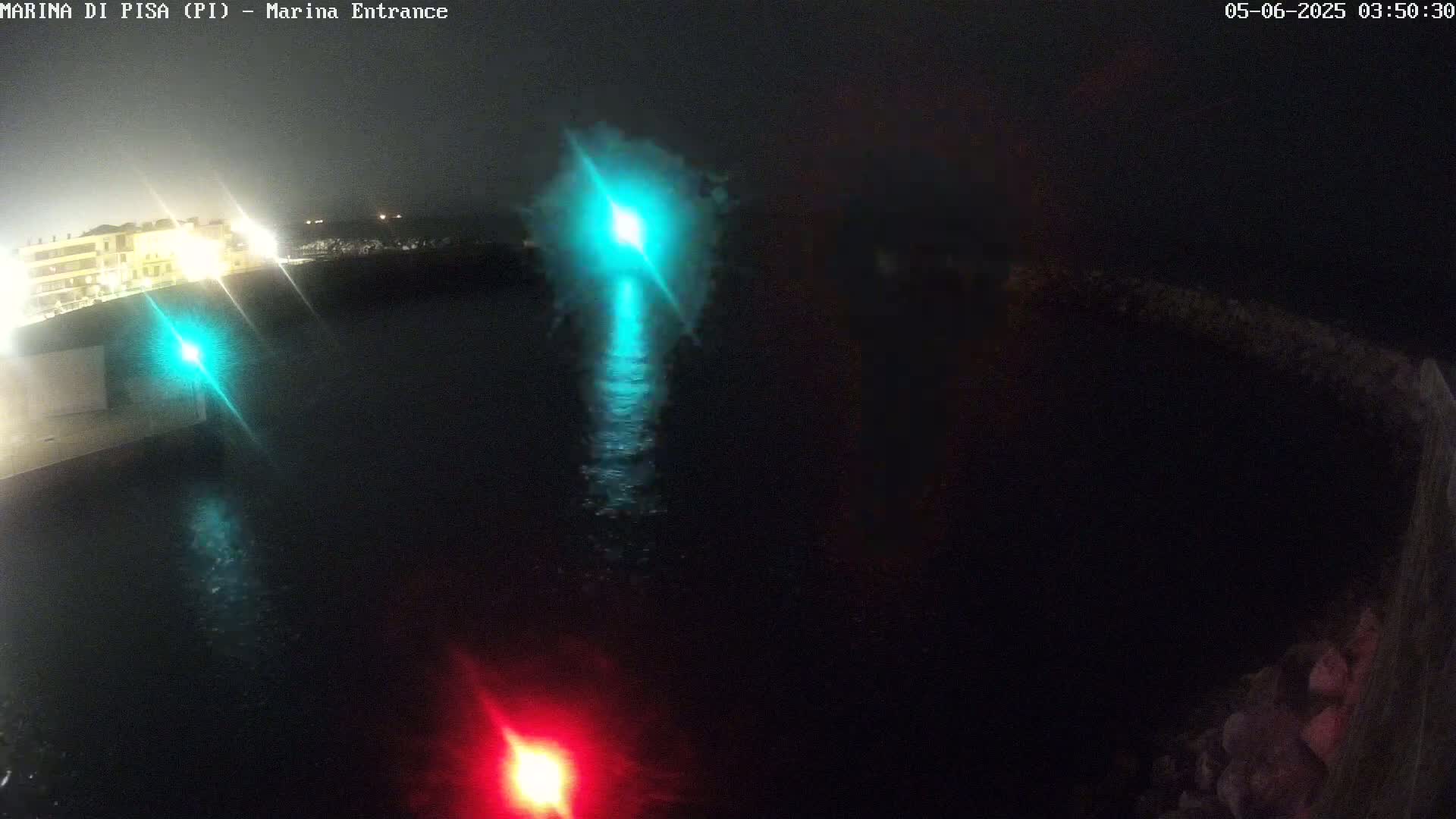 A nighttime view of a marina entrance with calm dark water reflecting lights from the shore and navigation lights.