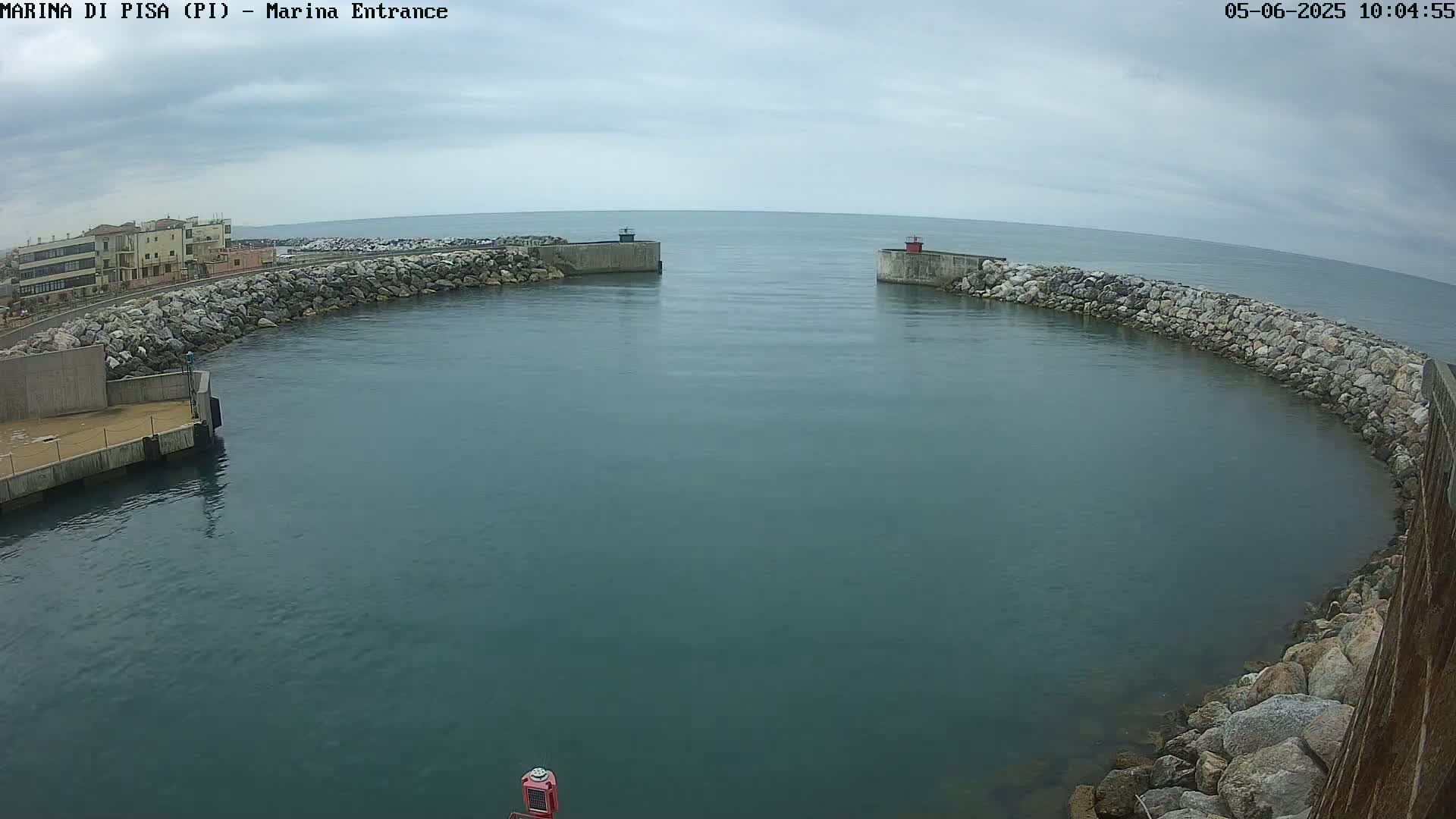 A calm, gray day shows a harbor entrance with stone walls and a small building in the background.