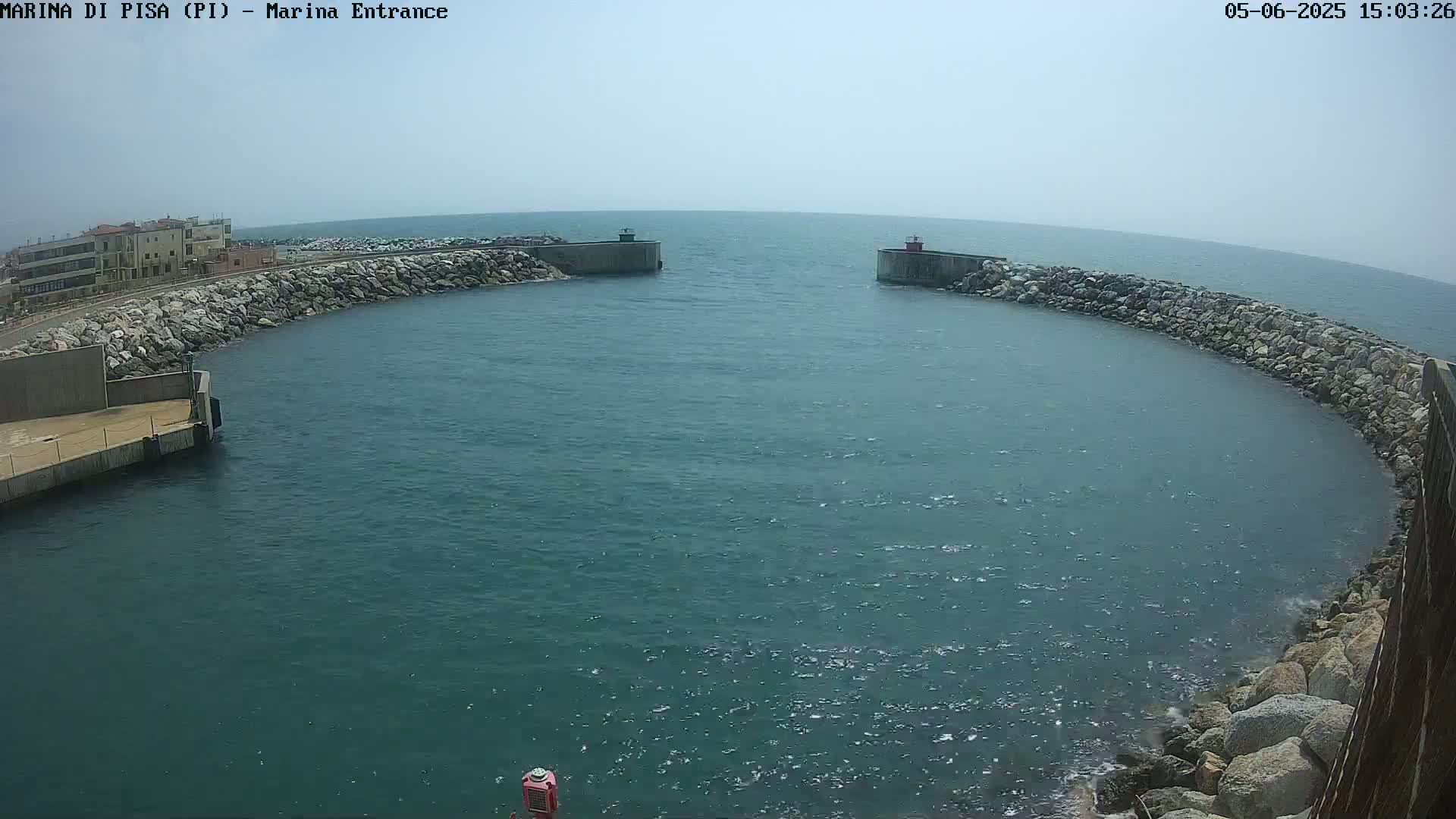 A calm, hazy day shows a harbor entrance with rocky breakwaters curving into a teal-colored sea.