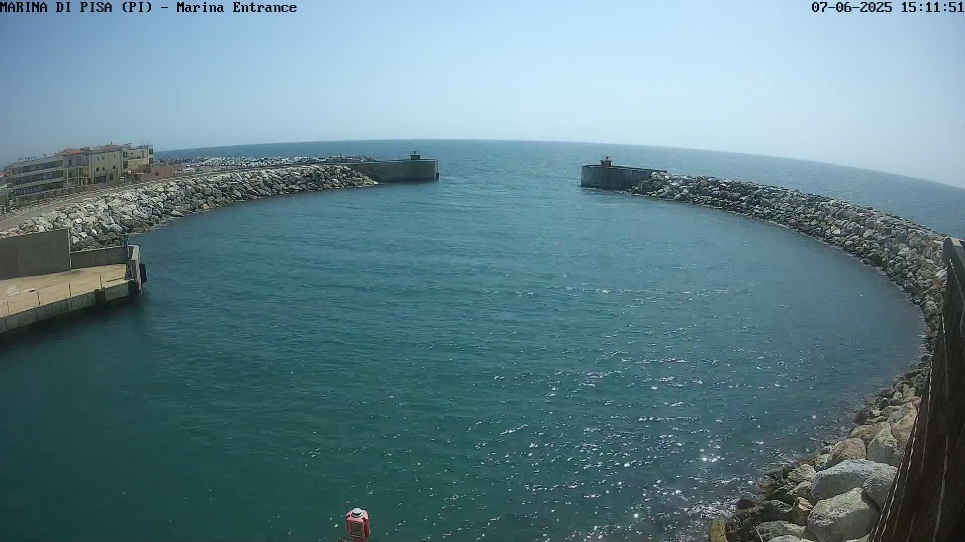 A marina entrance with calm, blue water is framed by rock walls on a sunny day.
