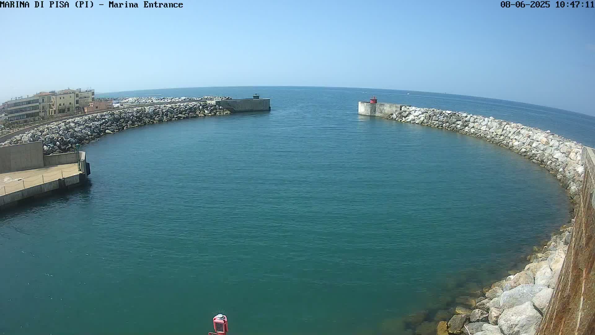 A harbor entrance with calm, teal water is enclosed by stone walls under a clear blue sky.