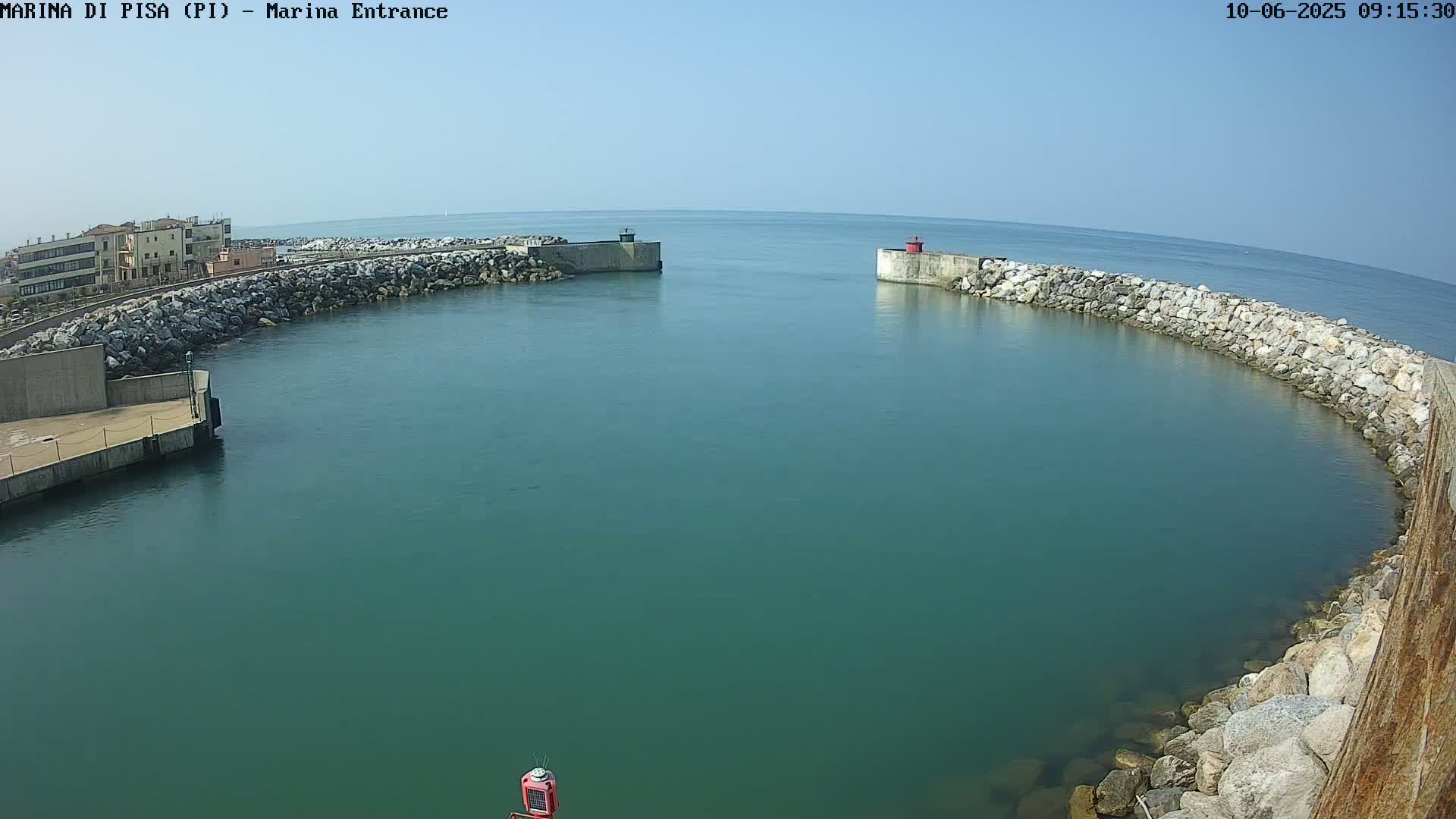 A harbor entrance with calm, teal water is enclosed by rock walls and concrete structures, under a clear blue sky.