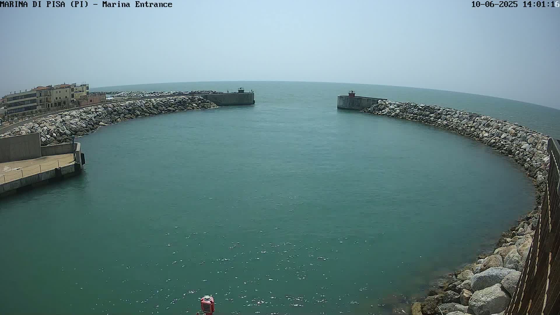 A marina entrance with calm, teal-colored water is framed by rocky walls under a clear, bright sky.