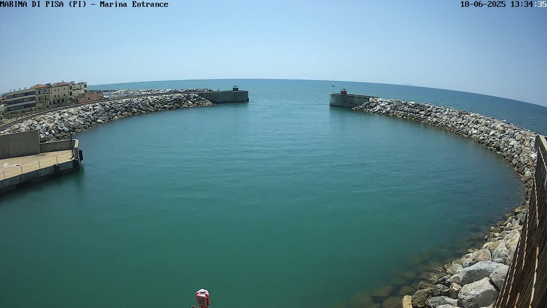 A harbor entrance with calm, teal water is framed by rock walls under a clear, sunny sky.