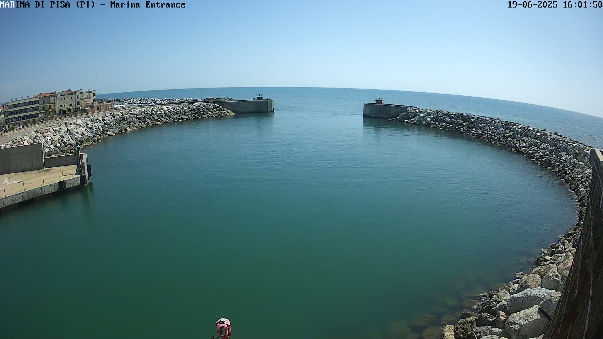 A calm, clear day reveals a harbor entrance, defined by two rock-lined walls curving into a teal-colored body of water.