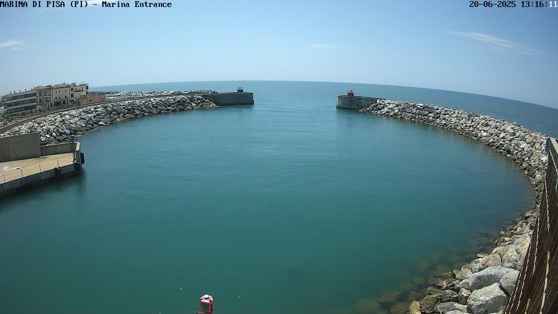 A harbor entrance with calm, teal water is framed by rock walls under a clear blue sky.