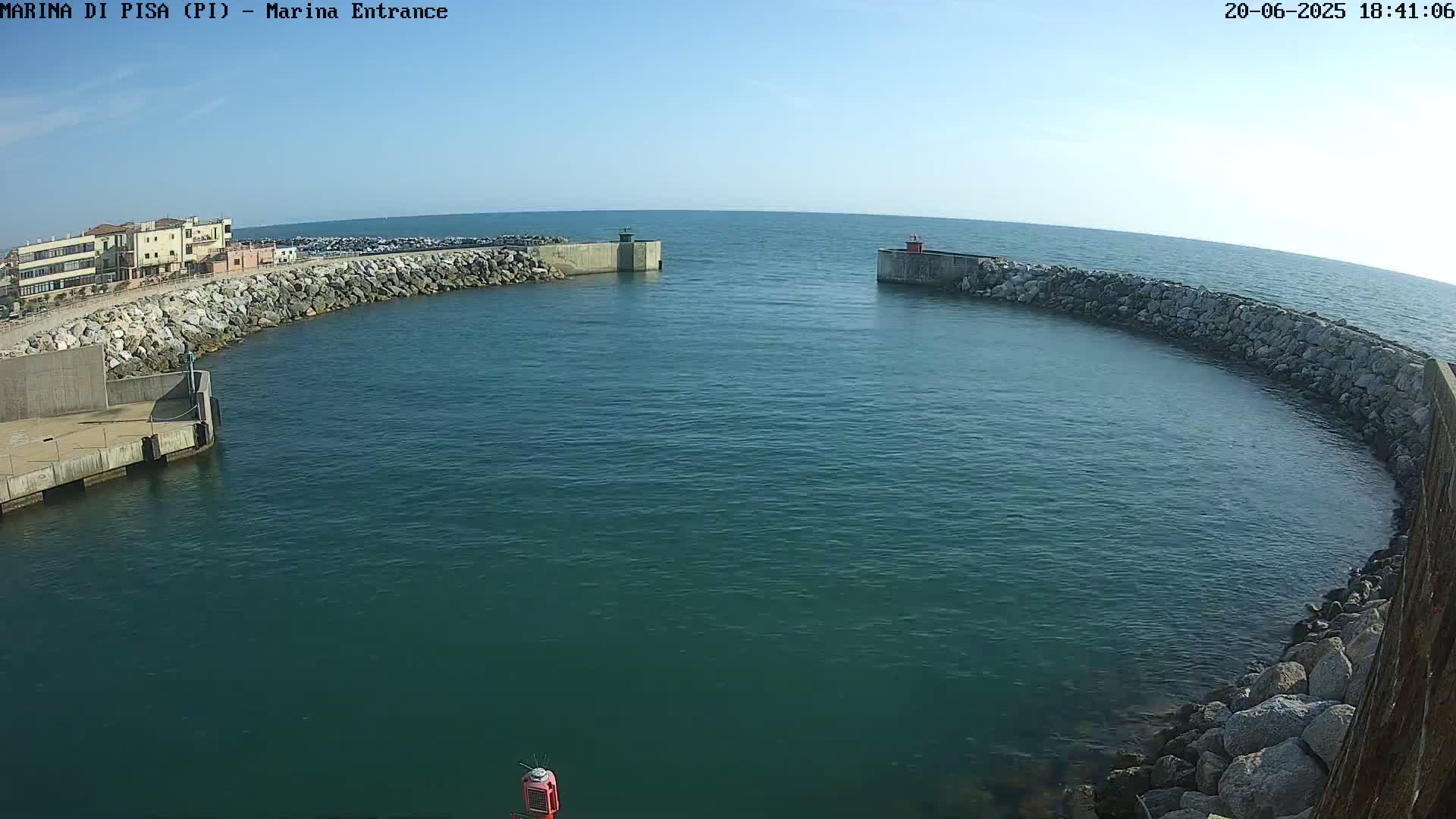 A calm, clear day reveals a harbor entrance with stone walls curving around a body of dark teal water.