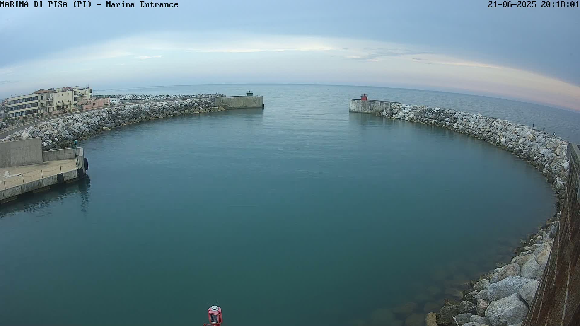 A calm, teal harbor is enclosed by stone walls under a mostly cloudy sky.