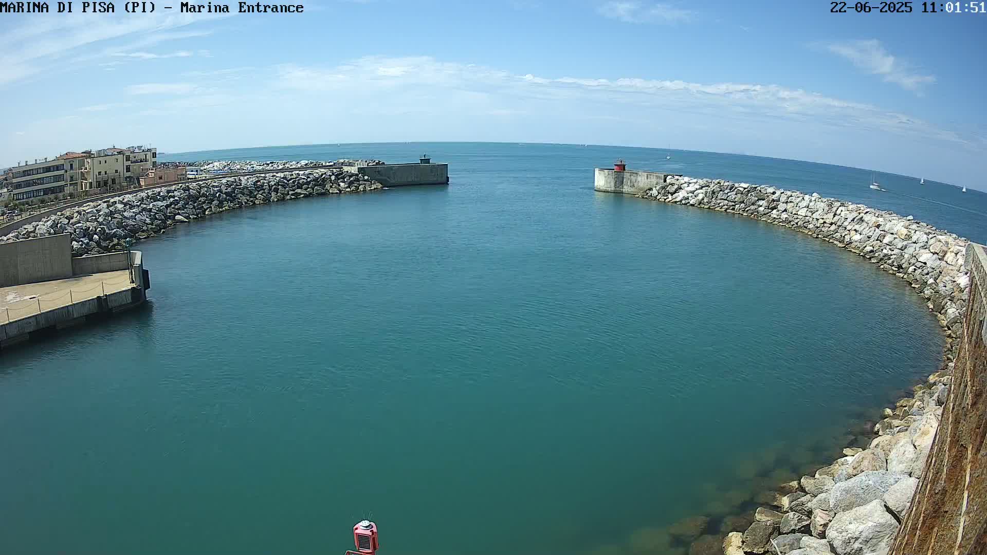 A harbor entrance with calm, teal water is bordered by rock walls under a mostly sunny sky.